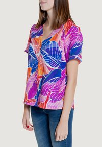 Camicia a maniche corte con bottoni, caratterizzata da una vivace stampa di foglie in tonalità di rosa, blu e arancione; tessuto leggero con una finitura texturizzata.