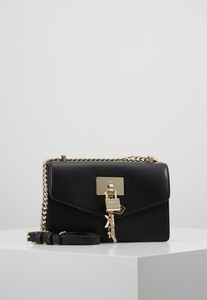 Sac bandoulière en cuir noir avec sangle chaîne dorée, serrure dorée et breloque clé sur le rabat avant, présenté sur une surface blanche.