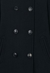 Cappotto in lana nera doppiopetto con tessuto testurizzato, dotato di sei bottoni rotondi e due tasche laterali.