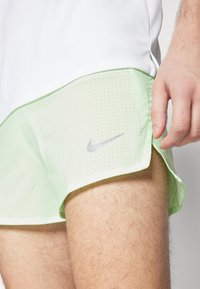 Nike sportshorts i ljusgrön med perforerad struktur, med en vit övre del och en silverfärgad Nike-logotyp på sidan.