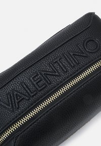 Pouch din piele neagră cu un logo „VALENTINO” embosat și un fermoar auriu, cu o suprafață texturată și o formă rotunjită.