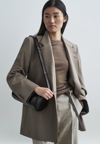 Beige oversized blazer, brown knit top, gray trousers, and dark textured handbag. Notable details: large sleeves, gold accents on belt, structured silhouette.