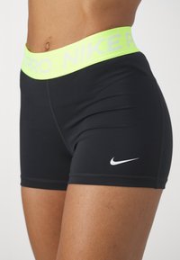 Zwarte Nike Pro shorts met een felgeel neonkleurige tailleband. Heeft een wit Nike-logo op de linker bovenbeen en een slank, aansluitend ontwerp.