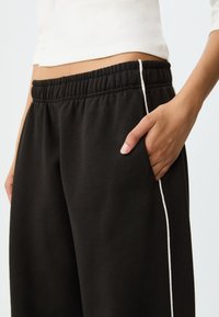 Zwarte joggingbroek met een elastische tailleband, zijzakken en witte biezen langs de buitennaad. Zachte stof met een comfortabele pasvorm.