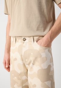 Beige cotton t-shirt with short sleeves, paired with beige camouflage pants featuring a button closure and side pockets.