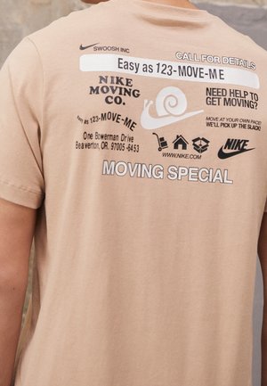 Beige bomulds T-shirt med grafiske tryk i sort og hvid, herunder tekst, et snegleikon og Nike-logoer. Korte ærmer og rund hals design.