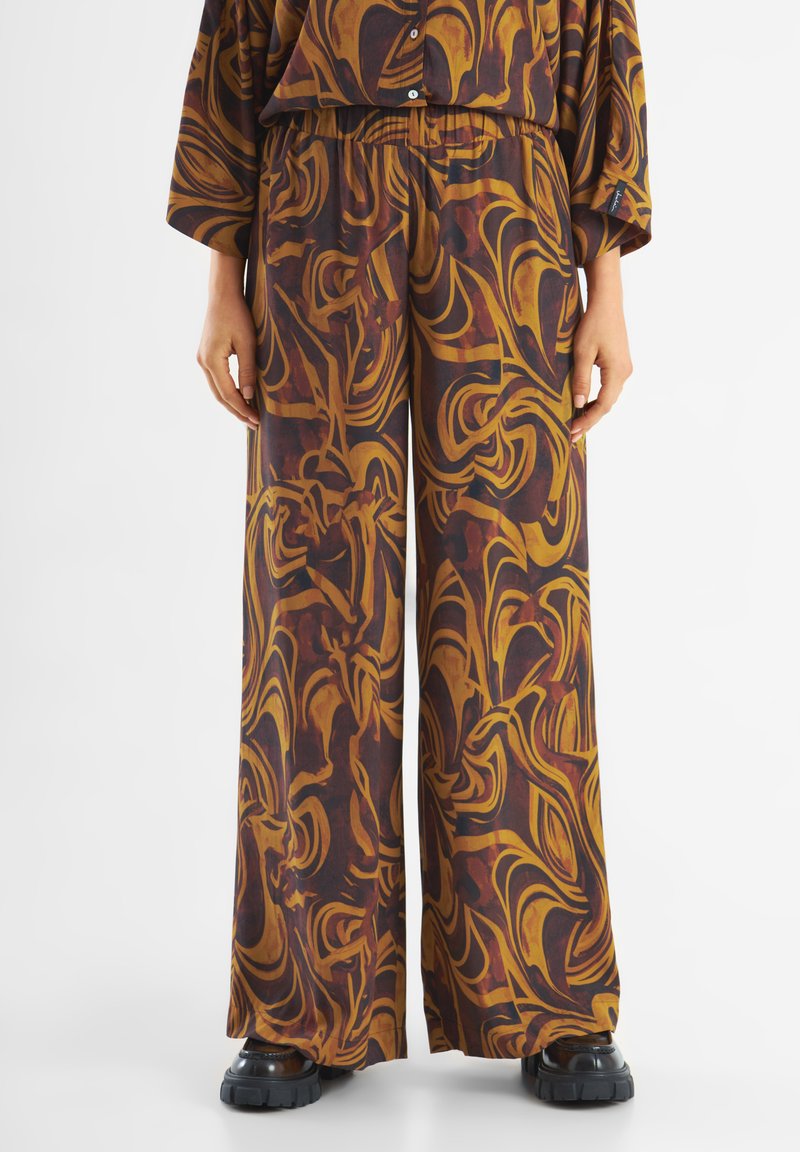 Pantalons évasés en tissu doux avec un motif abstrait tourbillonnant dans des tons sombres et chauds. Ceinture élastique avec coupe ample.