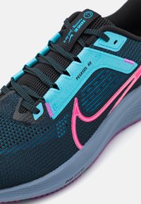 Scarpa da corsa Nike Pegasus 40 con una tomaia in mesh blu scuro, dettagli azzurri, logo rosa e suola grigia con una finitura texture.