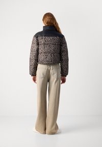 Puffjakke med leopardmønster og svarte ermer, med høy krage, parret med lyse beige vide bukser og hvite joggesko.