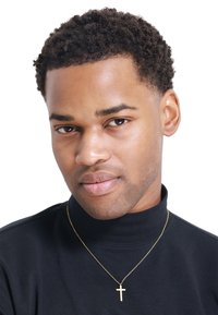 Un haut à col roulé noir avec une texture lisse, accompagné d'un collier en croix doré. L'arrière-plan est blanc, mettant en avant les traits du visage et les bijoux.