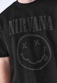 Black cotton t-shirt featuring rhinestone embellishments of "NIRVANA" text and a smiley face design with X-shaped eyes.