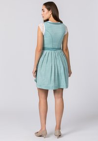 A back view of a turquoise dress with a textured pattern, lace cap sleeves, and a pleated skirt, paired with beige heels.
