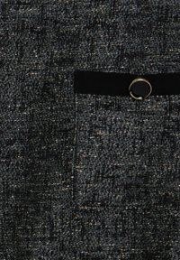 Tissu texturé noir et argent comportant une petite poche avec une sangle noire et une accent en métal doré.