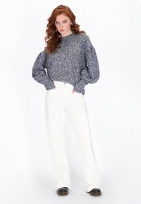 Grauer strukturierter Strickpullover mit puffigen Ärmeln, kombiniert mit hochtaillierten weißen weit geschnittenen Hosen und schwarzem Schuhwerk.