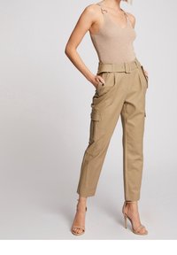 Brune cargobukser med belted talje, der har sidelommer og en skræddersyet pasform. Kombineret med en nude ribbet tanktop og strophæle.