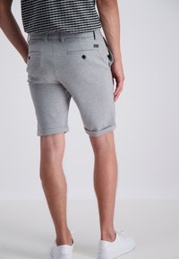 Pantaloni corti in misto cotone grigi con risvolti, due tasche posteriori con bottoni e design slim fit. Indossati con scarpe da ginnastica bianche.