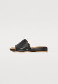 Black leather slide sandal with a wide upper band, tan sole, and slight heel, featuring a smooth texture and minimalist design.