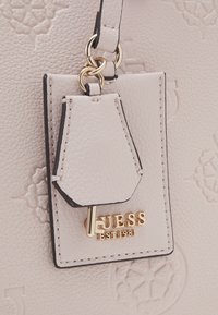 Borsa in pelle testurizzata beige chiaro con hardware dorato. Presenta un'etichetta a forma di chiave, logo impresso e dettagli in nero.