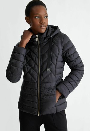 Giubbotto puffer nero con motivo a zigzag, chiusura a zip e cappuccio. Caratteristiche includono una cerniera dorata e dettagli con cordoncino regolabile.