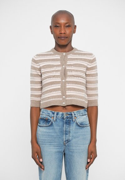 Giacquette beige courte avec des rayures texturées, dotée d'un col rond, de manches courtes et de boutons en perles, associée à un jean bleu clair.