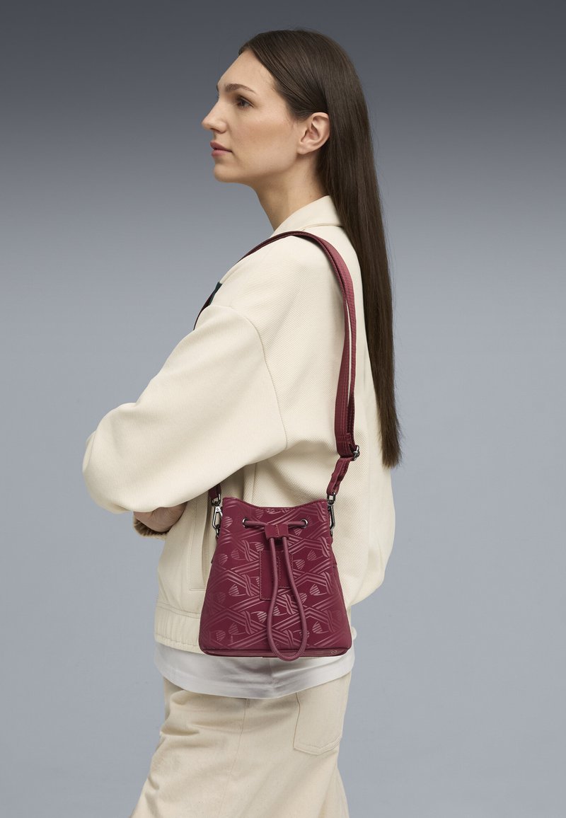 Bolso de cuero burdeos tipo bucket con patrón geométrico grabado, correa de hombro ajustable y cierre de cordón. Textura suave, diseño compacto.