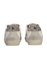 Un par de zapatillas beige con tacones plateados brillantes, logo de llamas negras, parches de ante en el talón y "GAMIN" grabado en las suelas de goma.