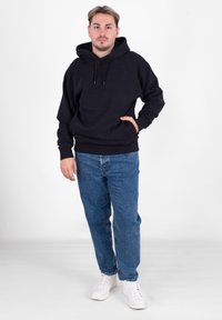 Czarna bluza z kapturem, wyposażona w przednią kieszeń i sznurek do regulacji kaptura, zestawiona z jasnoniebieskimi dżinsami i białymi trampkami. Gładki materiał, casualowy styl.