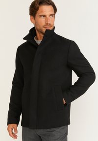 Sort uldblande frakke med høj krave, sidelommer og moderne snit. Har en glat tekstur og et minimalistisk design.