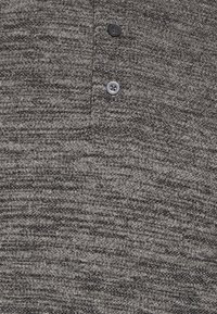 Tissu tricot marbré gris et noir avec deux boutons visibles sur une patte de boutonnage, montrant la texture et les détails des boutons.