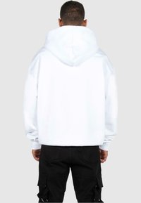 Biała bawełniana hoodie z dużym kapturem, ściągaczami przy mankietach i luźnym krojem, w połączeniu z czarnymi spodniami cargo. Brak widocznych logo lub wzorów.