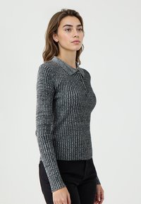 Langärmlige Bluse mit Kragen aus schwarzem und grauem Rippmaterial, ausgestattet mit einer Knopfleiste und taillierter Passform. Strukturierter Stoff mit dezentem Muster.