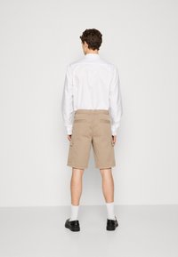 Pantaloni cargo beige con vestibilità rilassata, dotati di tasche laterali e una vita elasticizzata. Indossati con una camicia bianca a maniche lunghe e scarpe nere.