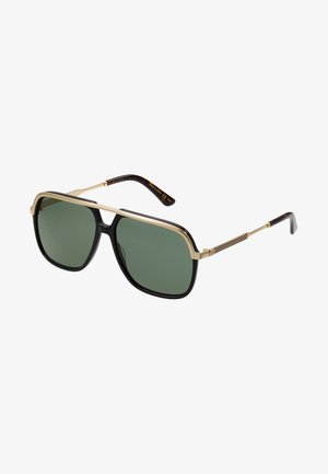 Gafas de sol rectangulares negras con lentes verdes, detalles dorados y un diseño de marco audaz, con lados gruesos y un acabado brillante.