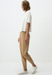 T-shirt blanc court à manches courtes associé à un pantalon tapered marron clair et des baskets blanches. Tissu lisse et coupe décontractée.