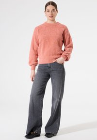 Suéter rosa de felpa con escote redondo y mangas largas, combinado con unos jeans de pierna ancha en gris oscuro y zapatos negros. Diseño simple y texturizado.