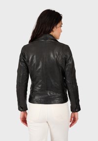 Veste en cuir noir au design ajusté, avec des détails de couture subtils et des boutons pression sur les poignets. Texture lisse avec une brillance.