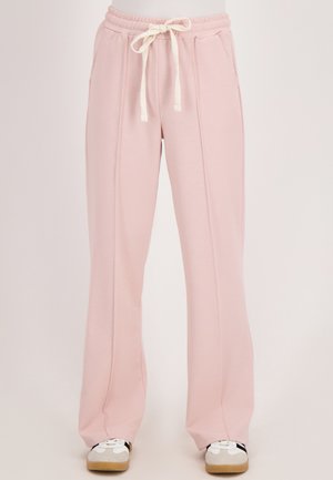 Lichtroze wijde sweatpants met een witte trekkoord in de taille en zijzakken, gedragen met witte en beige sneakers.