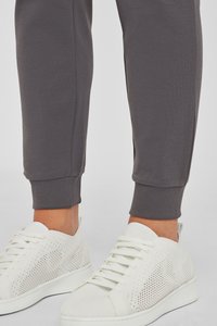Graue Trainingshosen mit gerippten Bündchen, kombiniert mit weißen Mesh-Sneakers, die eine durchgehende weiße Sohle und eine perforierte Oberseite für Atmungsaktivität aufweisen.