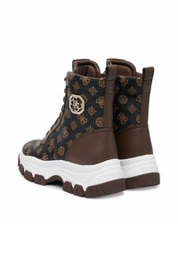 Un paio di sneaker alte marroni e nere con stampa logo a motivo, suole bianche spesse ed emblema metallico sul lato.