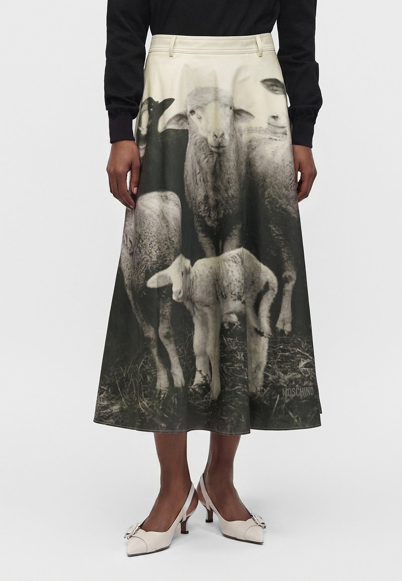 Femme portant une jupe taille haute avec un imprimé noir et blanc de plusieurs moutons debout sur l'herbe, associée à des talons blancs et un haut noir.