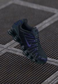 Melnas un purpursarkanas sporta apavi ar teksturētu sieta augšdaļu, izliekta zole un kontrastējošiem akcentiem. Aprīkoti ar saitēšanas sistēmu un izteiktu zīmolu.