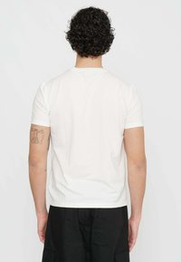 T-shirt bianca in cotone con maniche corte, scollatura rotonda, texture liscia e forma aderente, indossata da una persona vista di spalle.