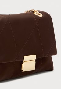 Clutch in finta pelle marrone con un motivo geometrico trapuntato, accessori in oro e chiusura a scatto. Dettaglio a catena attaccato per il trasporto.