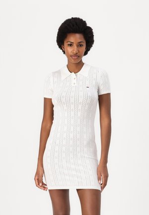 Robe en tricot blanc avec un col polo, des manches courtes et des motifs verticaux avec des détails en œillets. Coupe ajustée avec un logo de marque subtil.