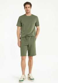 Camiseta de algodón verde oliva y pantalones cortos a juego con una cintura ajustable, combinados con zapatillas beige y verdes. Diseño simple y de corte relajado.