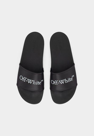Ζευγάρι μαύρα σανδάλια τύπου slide με λογότυπο Off-White™ σε λευκό στα λουράκια, τοποθετημένα πάνω σε απλό ανοιχτόχρωμο φόντο.
