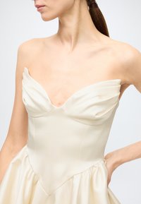 Strapless cream dress with pleated bodice, smooth texture, fitted waist, and voluminous skirt; details include a heart-shaped neckline.