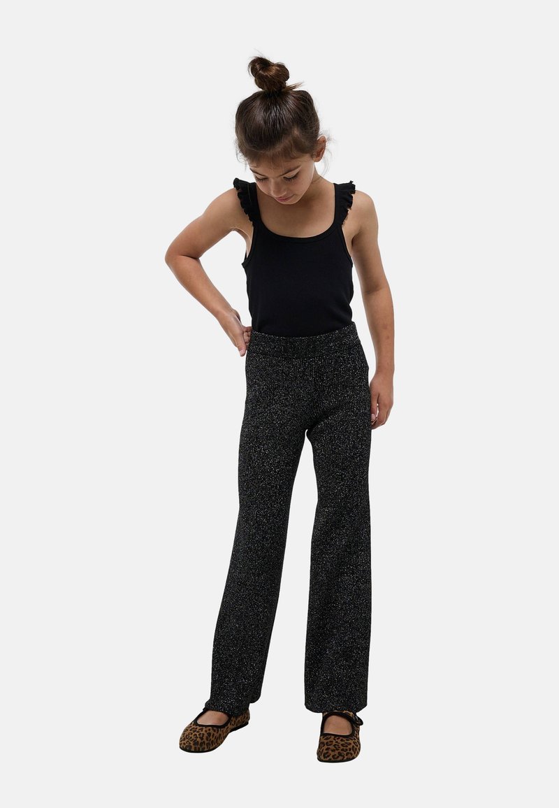 Débardeur noir côtelé avec bretelles à volants, associé à un pantalon noir à jambes larges avec un motif métallique tacheté et des ballerines imprimé léopard.