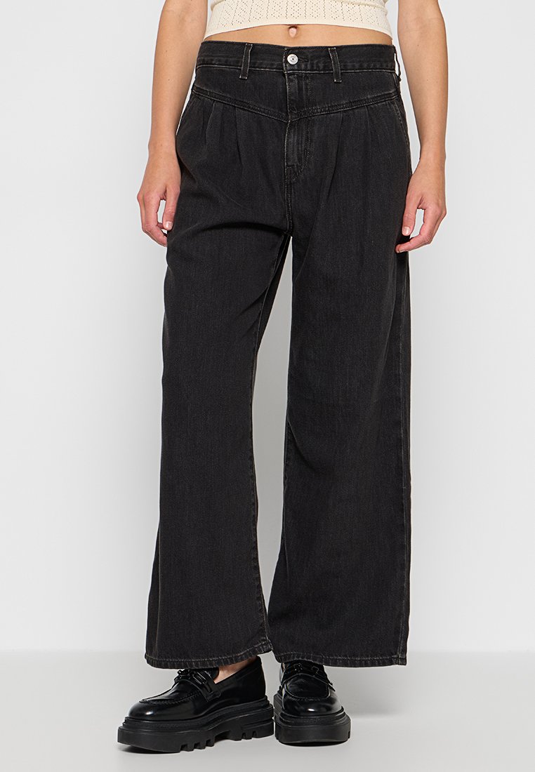 Jeans larges noirs en denim, avec une taille haute, un devant plissé et une fermeture classique à bouton et fermeture éclair. Texture lisse.