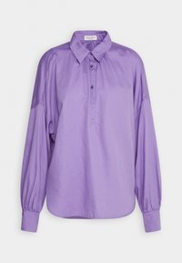 Blouse lavande à manches longues avec col boutonné, deux boutons près du cou et poignets élastiqués, présentée sur fond blanc.